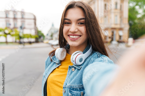 Image of woman with headphones smiling and taking selfie on cellphone