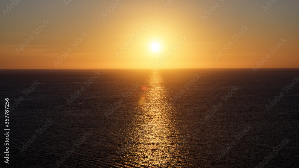 marvelous bright yellow sunlight reflected in calm endless ocean creating sun path under clear sky with orange disk in evening