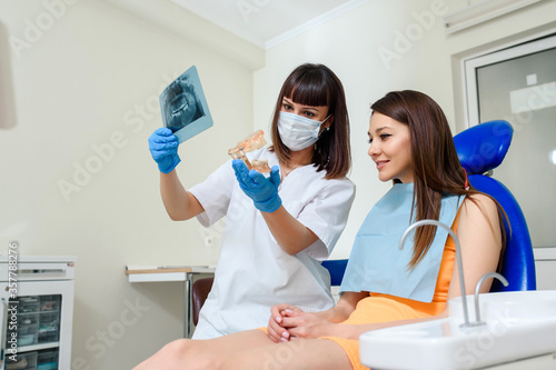 Young woman dentist explaining to her patient on a dental x-ray panoramic radiography all the dental treatment that needs to do in dentistry