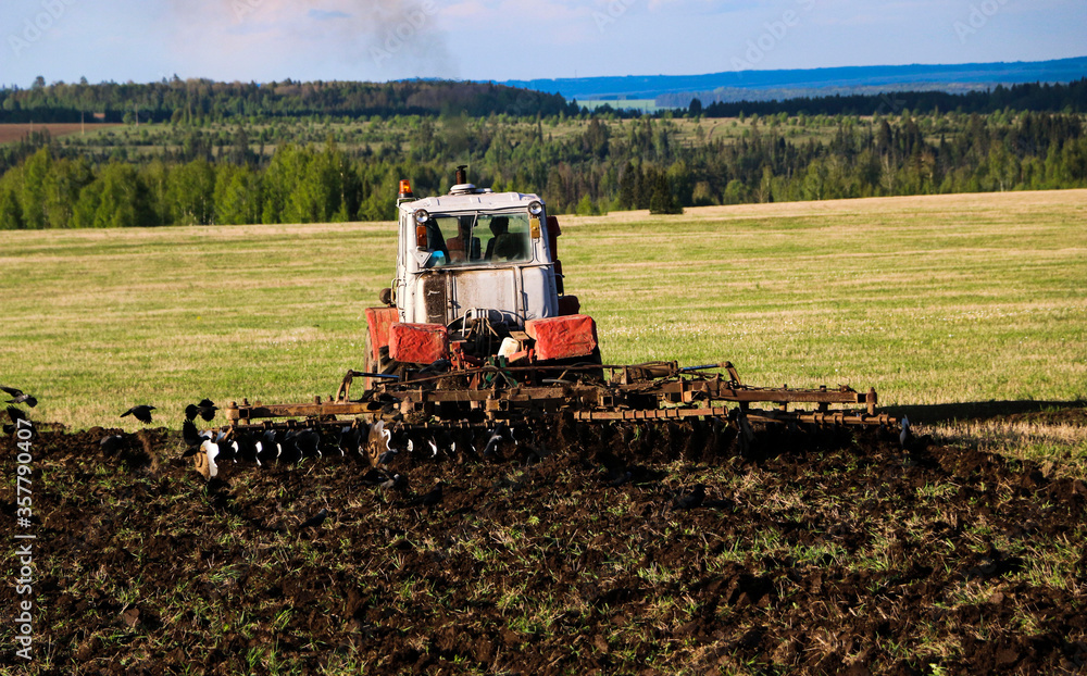 Fototapeta premium tractor plows and harrows land in large field on sunny spring day. preparing soil for planting crops, plowing soil with tractor with disk plow.