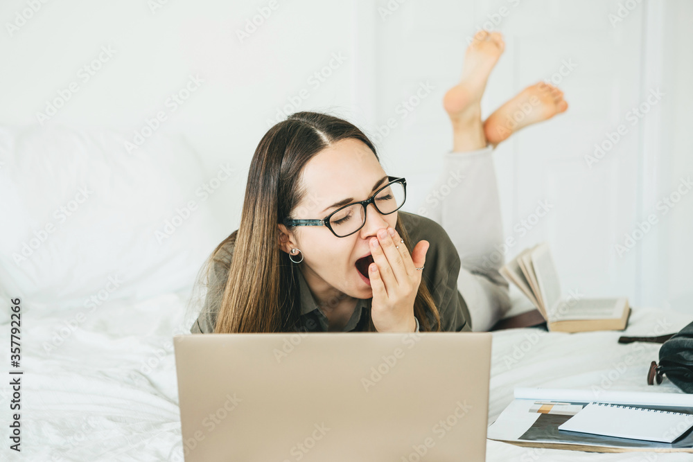 Girl yawns while working at a laptop. She is tired or overworked or has insomnia. Girl yawns while working at a laptop. She is tired or overworked or has insomnia.