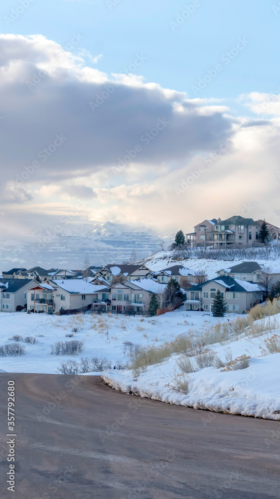 Vertical crop Curving road on snowy mountain setting with houses against cloudy blue sky