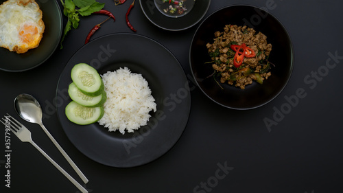 Stir fried minced pork with basil (Pad ka prao), rice fried egg serving on black ceramic plate and silverware