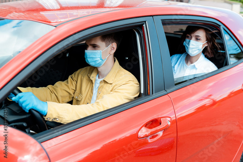male driver and woman in medical masks and gloves in taxi during covid-19 pandemic