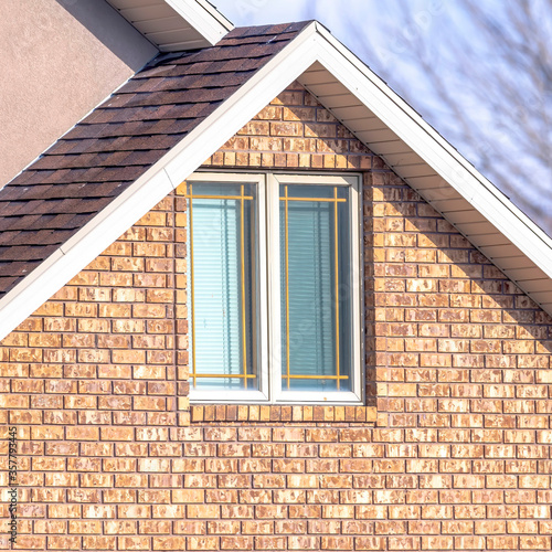 Square frame Close up of a home exterior with sunlit pitched roof over window and brick wall