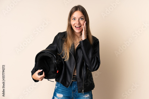 Young Lithuanian woman holding a motorcycle helmet isolated on beige background with surprise and shocked facial expression