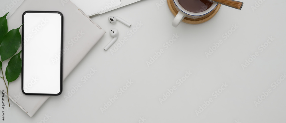 Copy space on white worktable with mock-up smartphone, wireless earphones, schedule book and hot cocoa cup - obrazy, fototapety, plakaty 
