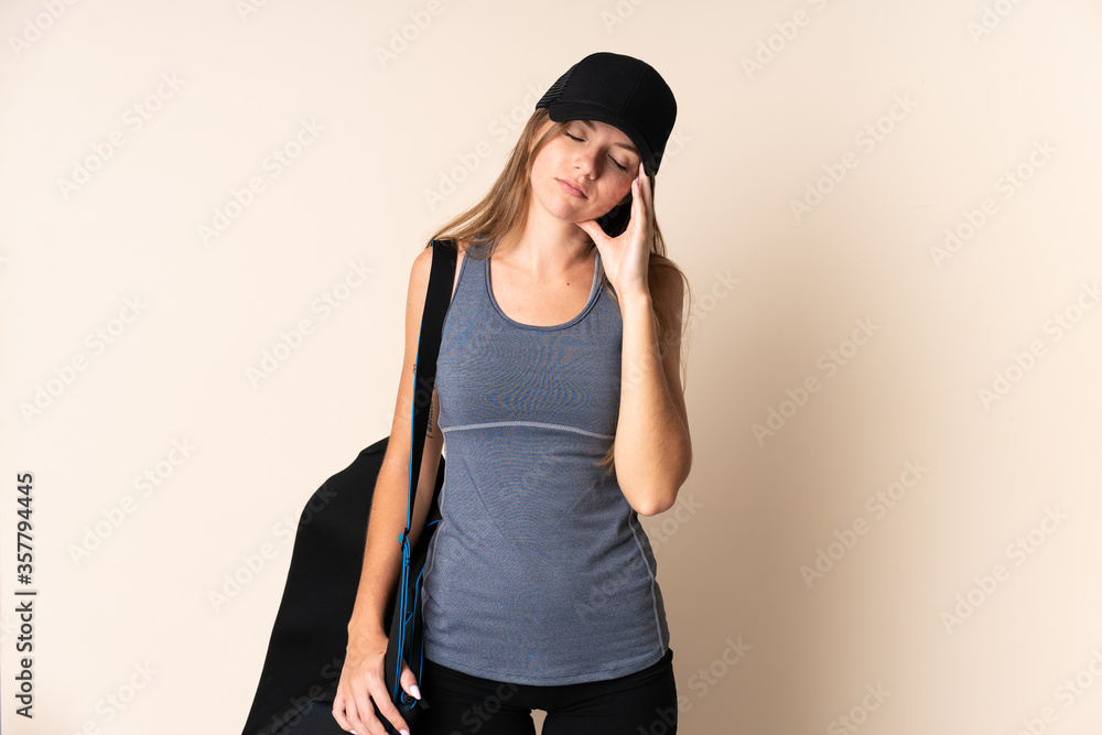 Young sport Lithuanian woman holding a sport bag isolated on beige background with headache Young sport Lithuanian woman holding a sport bag isolated on beige background with headache