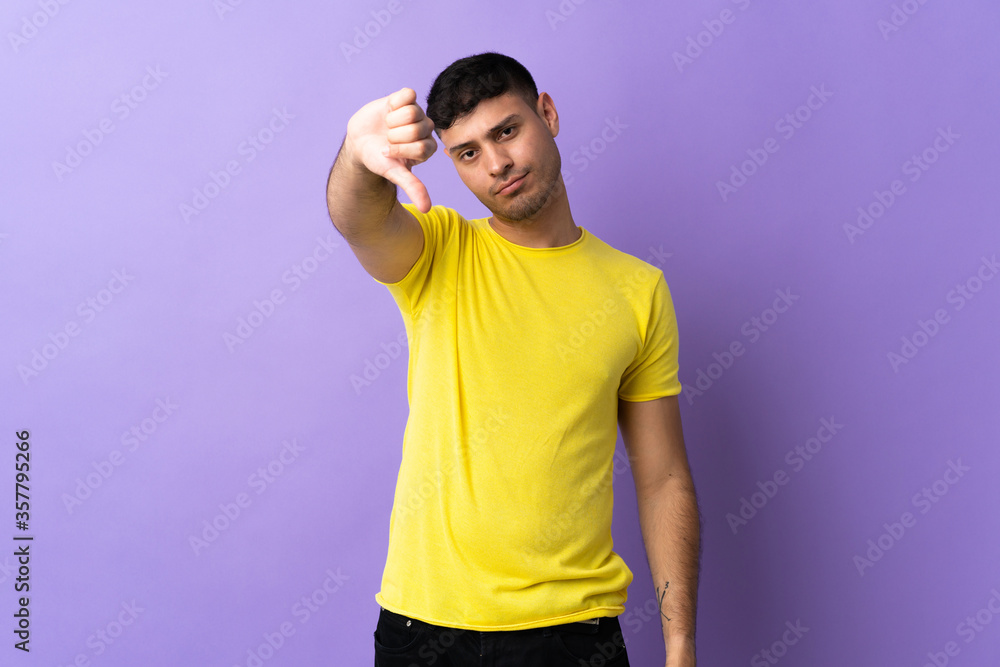 Young Colombian man isolated on purple background showing thumb down with negative expression Young Colombian man isolated on purple background showing thumb down with negative expression