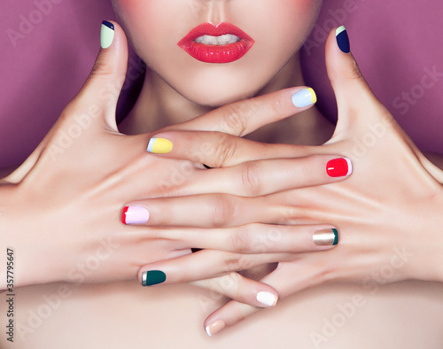 Beautiful female pink lips and hand with colorful manicure on nails with makeup closeup