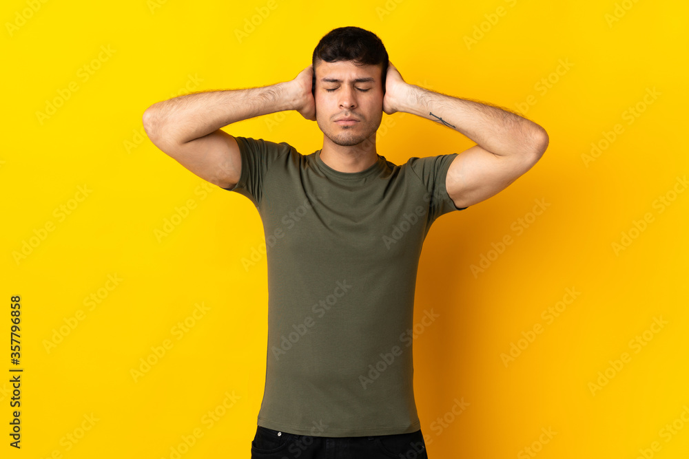 Young Colombian man isolated on yellow background frustrated and covering ears Young Colombian man isolated on yellow background frustrated and covering ears