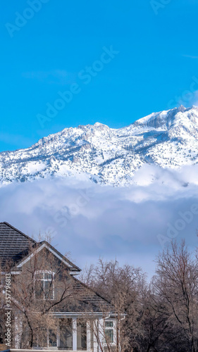 Vertical frame Sunlit snowy mountain with peak over low gray clouds against vibrant blue sky