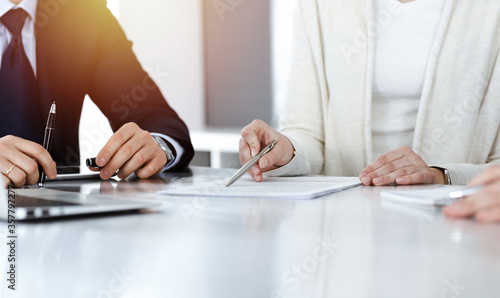 Business people discussing contract while working together in sunny modern office. Unknown businessman and woman with colleagues or lawyers at meeting