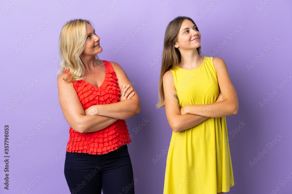 Mom and daughter isolated on purple background looking up while smiling Mom and daughter isolated on purple background looking up while smiling