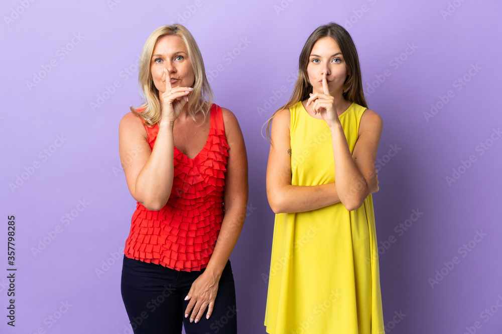 Mom and daughter isolated on purple background showing a sign of silence gesture putting finger in mouth Mom and daughter isolated on purple background showing a sign of silence gesture putting finger in mouth
