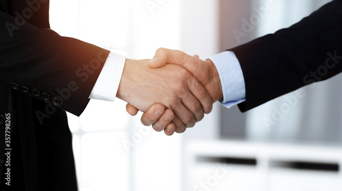 Business people shaking hands after contract signing while standing in sunny office. Teamwork and handshake concept