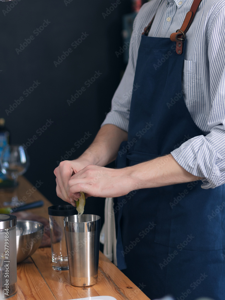 A man cook in a blue apron is cooking in the kitchen, the process of preparing a cocktail