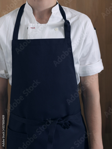 Fototapeta Man cook in blue apron and white shirt on a wooden background
