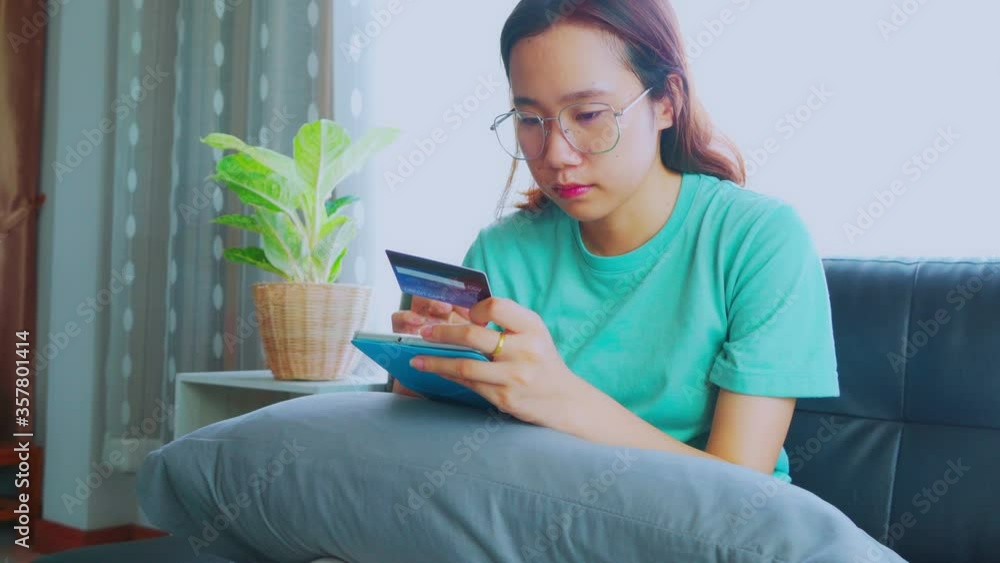 Young Asian woman sitting on a sofa holding a credit card while using a mobile device to type the credit card code Buy products online.
Young Asian woman sitting on a sofa holding a credit card while using a mobile device to type the credit card code Buy products online.