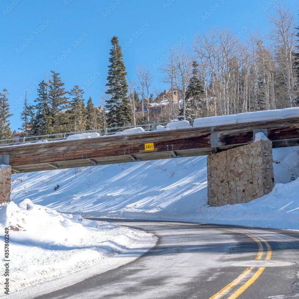 Square frame Paved road and snowy bridge on a hill with deep layer of sunlit snow in winter Square frame Paved road and snowy bridge on a hill with deep layer of sunlit snow in winter