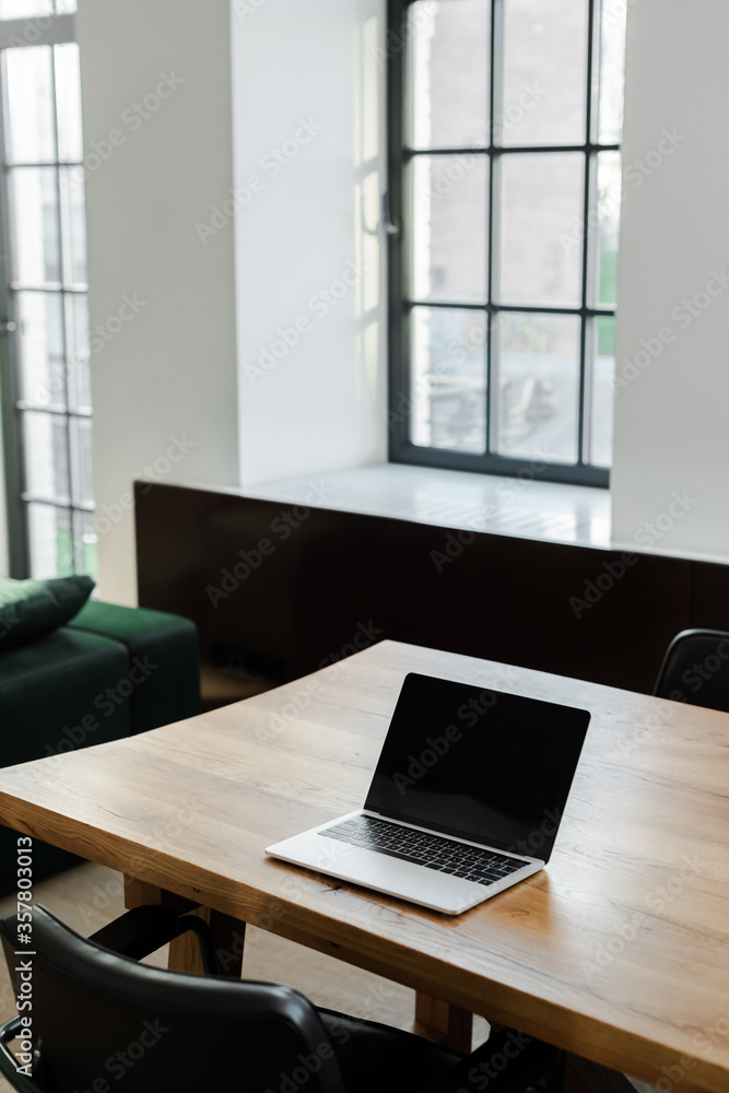 Fototapeta premium laptop with blank screen standing on table at home with window