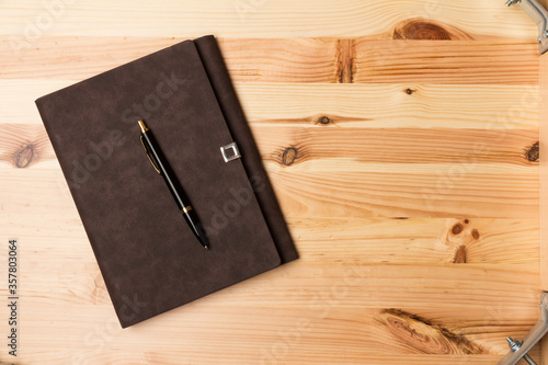Leather-bound business notebook with a pen on wooden background.