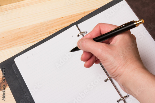 Leather-bound business notebook with a business pen in hand on wooden background.