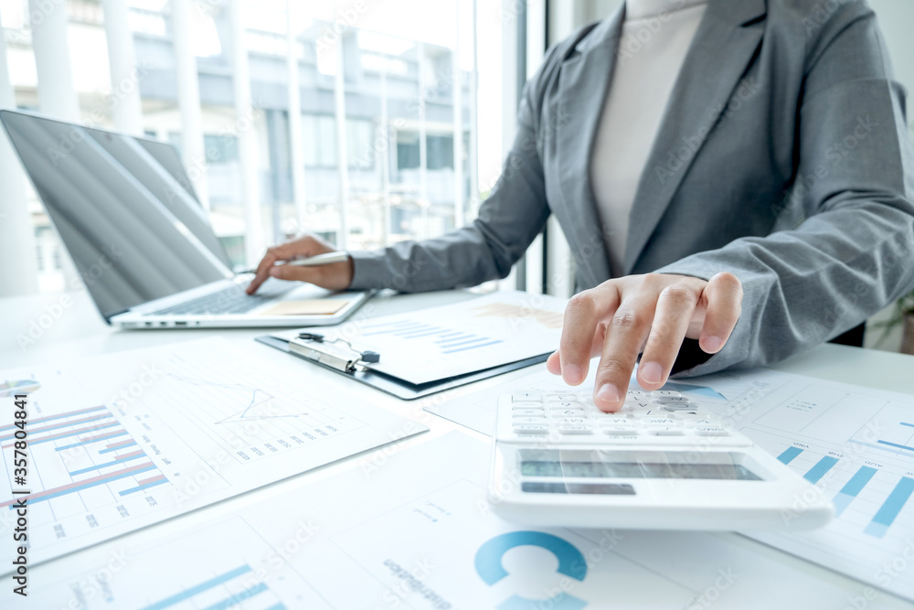 Business woman uses a calculator to calculate financial graphs that show results and analyze financial arrangements for business investment Business woman uses a calculator to calculate financial graphs that show results and analyze financial arrangements for business investment