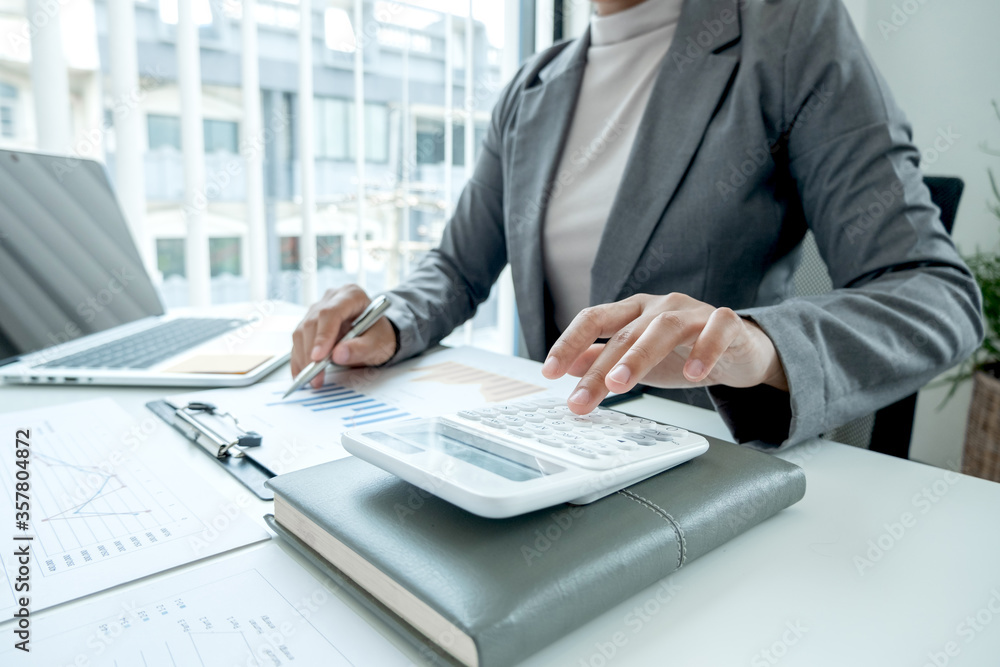Business woman uses a calculator to calculate financial graphs that show results and analyze financial arrangements for business investment Business woman uses a calculator to calculate financial graphs that show results and analyze financial arrangements for business investment