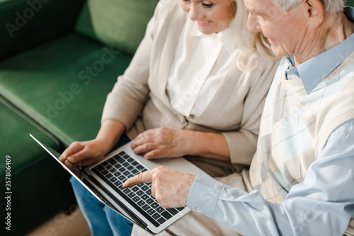 happy elderly couple pointing and having video chat on laptop at home during self isolation