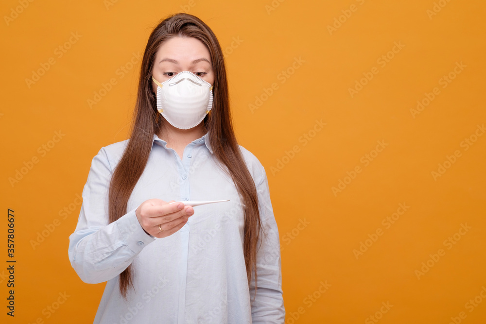 woman in medical mask on yellow background, coronavirus pandemic, woman looks at thermometer, emotions