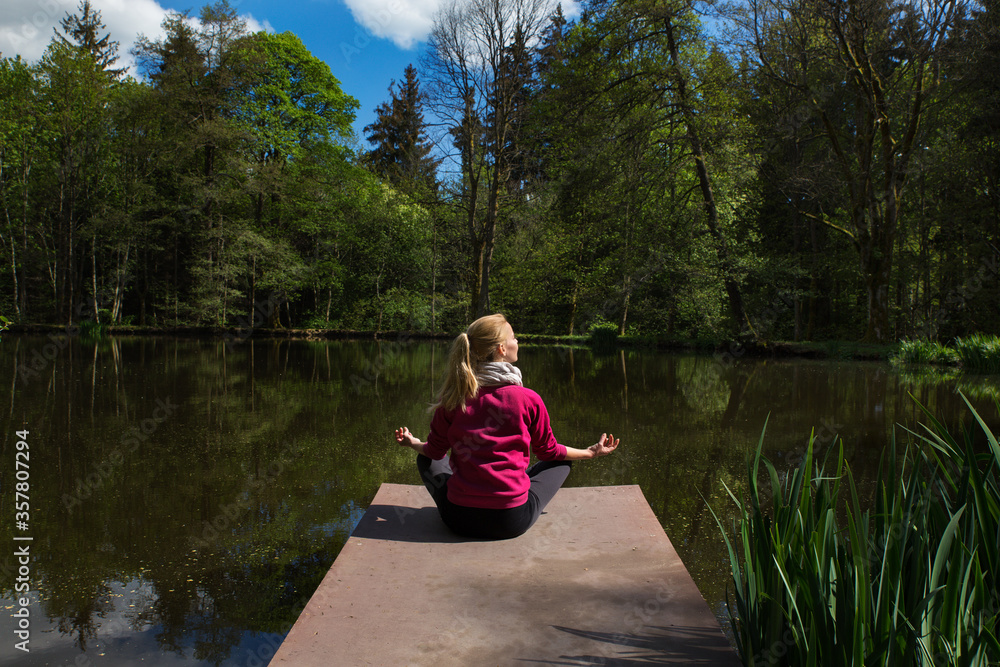Young woman sitting alone on dock by lake in lotus pose. Self-isolation in the open air Young woman sitting alone on dock by lake in lotus pose. Self-isolation in the open air