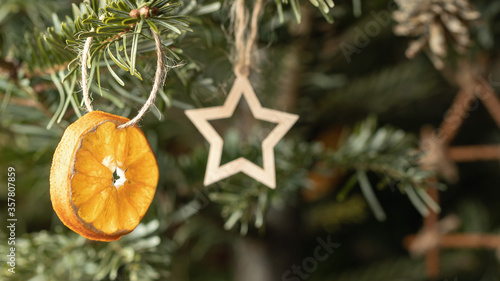 Zero waste christmas concept. Christmas tree decorated with ornaments made of natural materials - a slice of dried orange and wooden figures, close-up