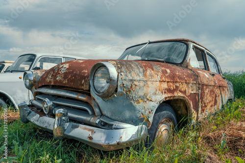 Old retro rusty abandoned car in green field.