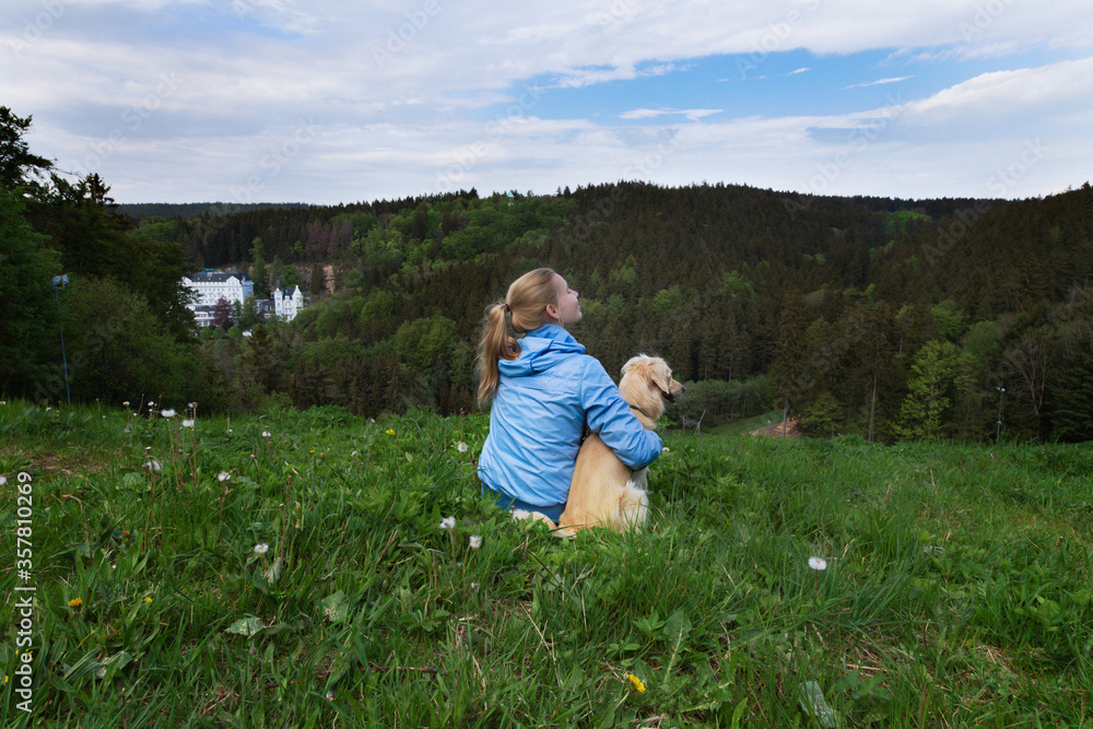 Young woman sitting on the grass with a dog in nature. Woman sitting on the hill with a dog overlooking hills.