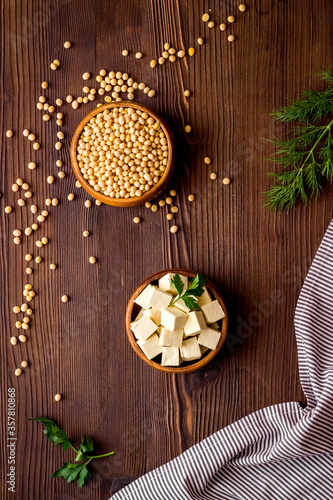 Tofu cubes in bowl and soybeans on wooden kitchen table top-down