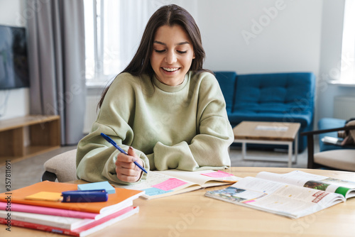 Photo of cheerful beautiful student woman smiling while doing homework