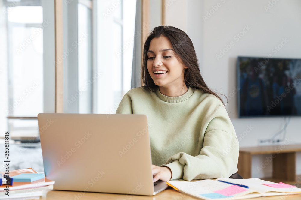 Photo of cheerful student woman using laptop while doing homework Photo of cheerful student woman using laptop while doing homework