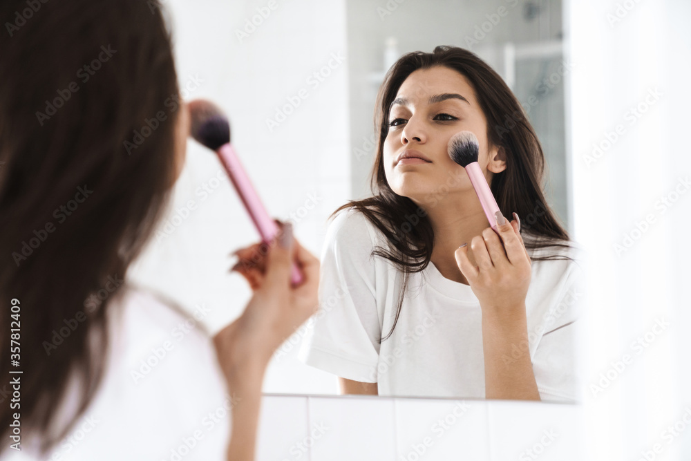 Photo of pleased woman using powder brush while looking at mirror Photo of pleased woman using powder brush while looking at mirror