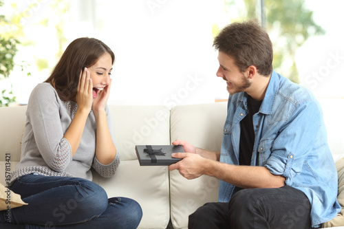 Excited woman receiving gift box from man at home