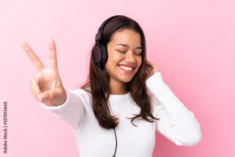 Fototapeta premium Young woman with earphones over isolated pink wall