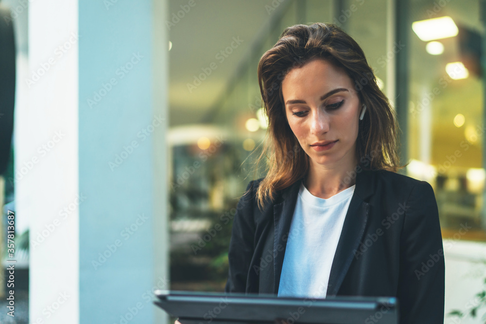 Successful female banker using tablet and wireless earphones outdoors near his office background lights, portrait young woman professional manager working on touch pad evening city Successful female banker using tablet and wireless earphones outdoors near his office background lights, portrait young woman professional manager working on touch pad evening city