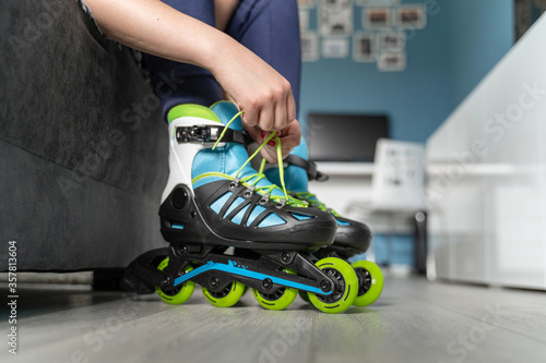 close up on foot of unknown caucasian woman on the floor taking off or putting on the rollerblade inline skates tying laces while sitting on bed at home in day fun freedom motion and youth concept photo