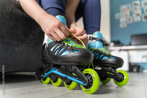 close up on foot of unknown caucasian woman on the floor taking off or putting on the rollerblade inline skates tying laces while sitting on bed at home in day fun freedom motion and youth concept photo