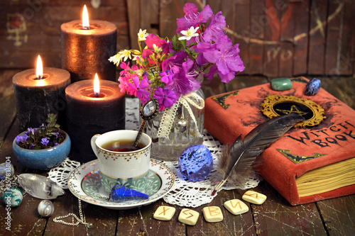 Romantic still life with cup of tea  witch book  runes and black candles.