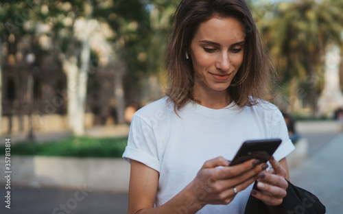 woman reading the financial news using a smartphone. Portrait of a girl browsing social networks or exchanging messages with friends on mobile phone enjoying summer in a city Park..