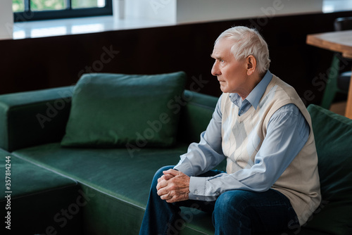 sad lonely elderly man sitting on sofa during self isolation photo