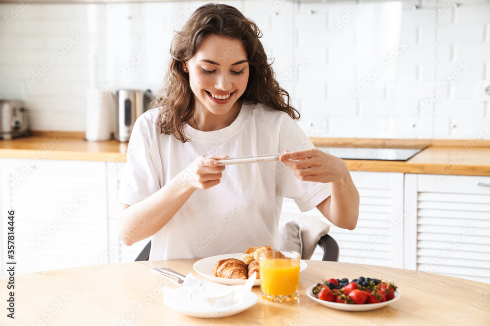 Photo of woman taking photo on cellphone while having breakfast