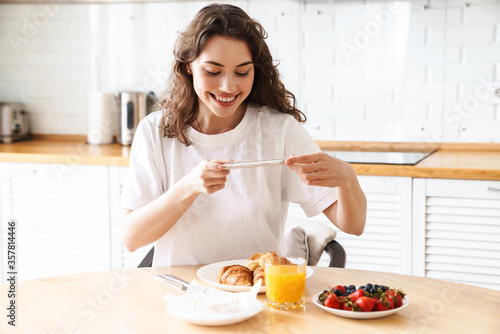 Photo of woman taking photo on cellphone while having breakfast