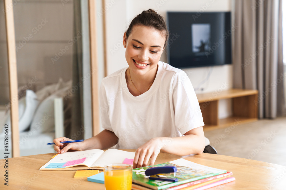 Photo of cheerful beautiful student woman smiling while doing homework